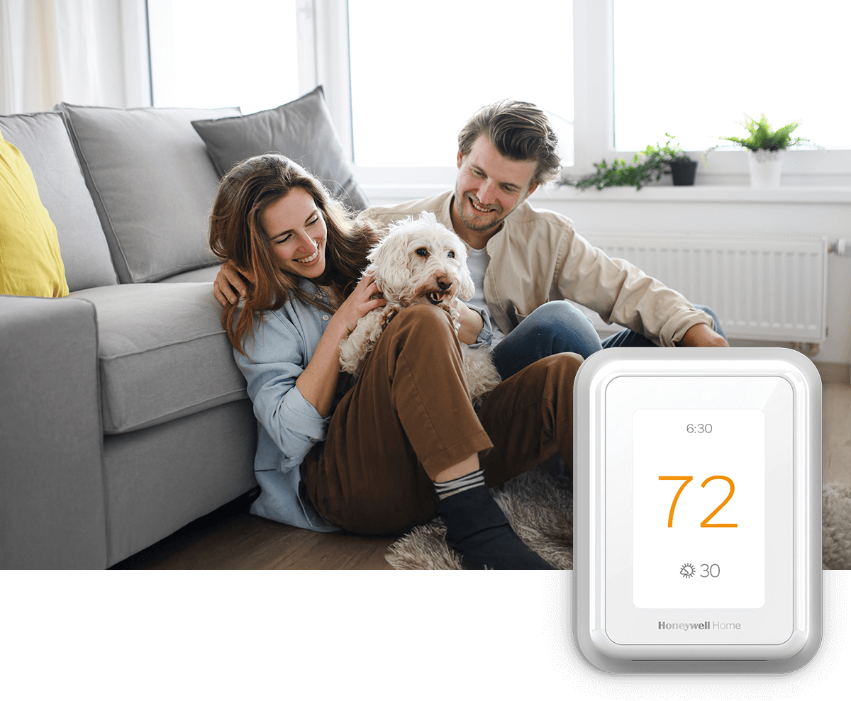 A smiling couple sit on the floor with their dog; a thermostat image is in the foreground