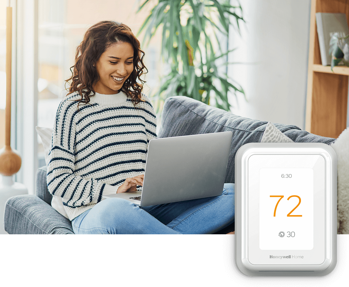 A young woman smiles while using her laptop on a sofa in a bright room; a thermostat image is in the foreground