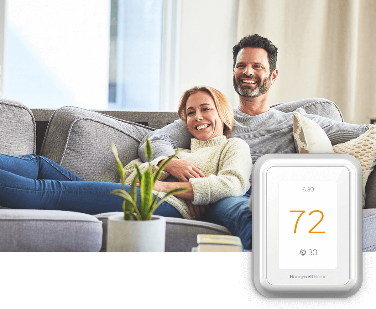A happy couple relaxes on a sofa, laughing; a thermostat image is in the foreground