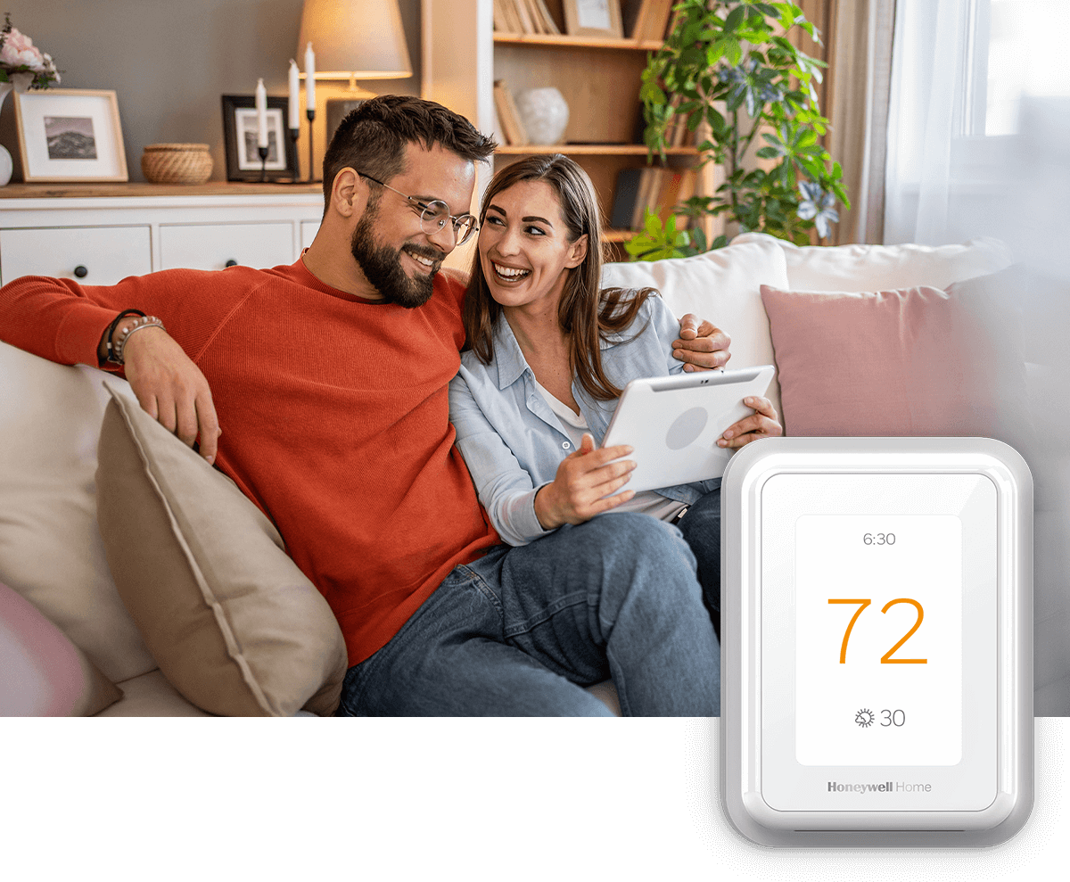 A smiling couple relaxes on the sofa, tablet in hand; a thermostat image is in the foreground