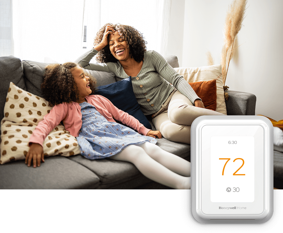 A mother and her daughter laugh on a sofa in a bright room; a thermostat image is in the foreground