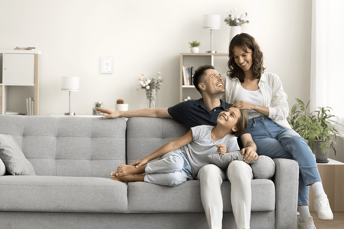 A living room with pillows on a sofa, a plant, modern ceiling light, and a wall thermostat