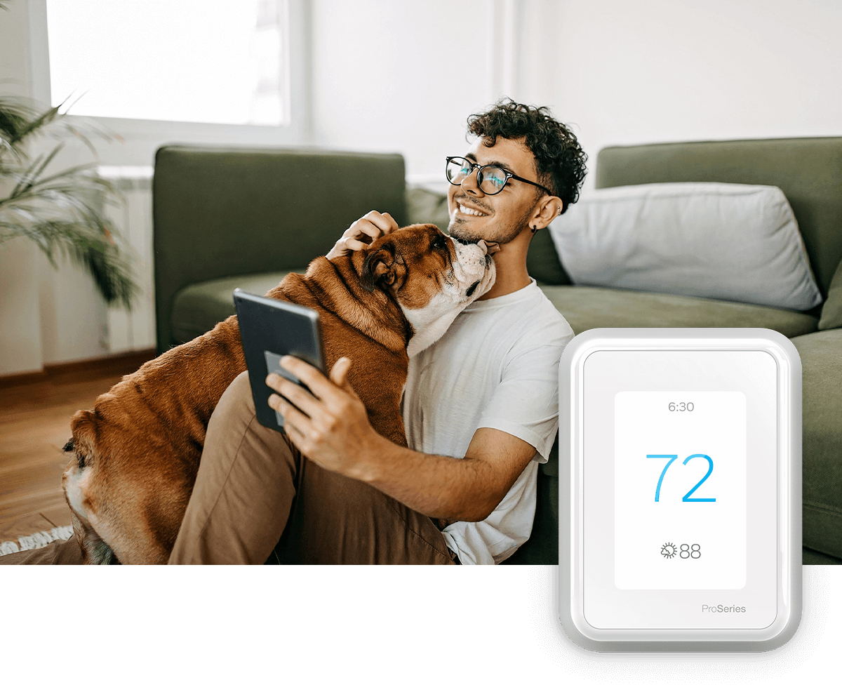 A young woman smiles while using her laptop on a sofa in a bright room; a thermostat image is in the foreground