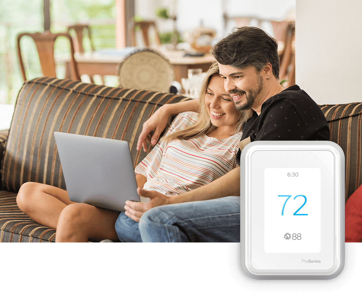 A young couple enjoys something on a laptop while seated on sofa on a bright day; a thermostat image is in the foreground