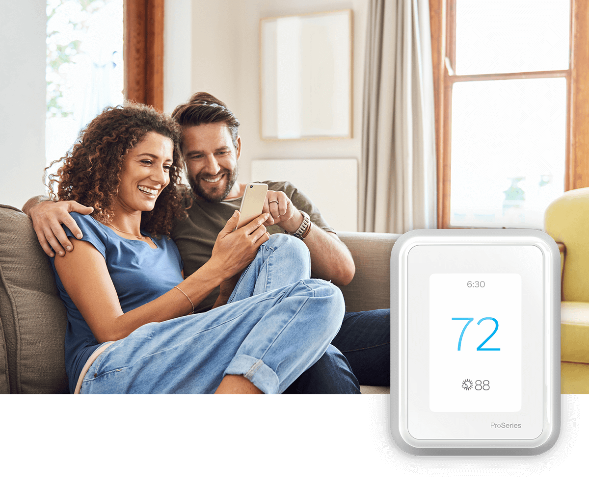 A young couple relaxes on a sofa, interacting with a smart phone in a bright room; a thermostat image is in the foreground