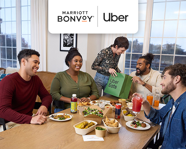 People gathered around a dinner table while a woman holds a green Uber Eats bag.