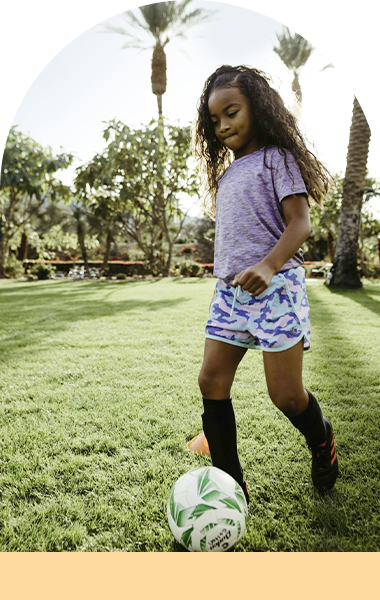 Young girl is playing soccer in a grassy field.