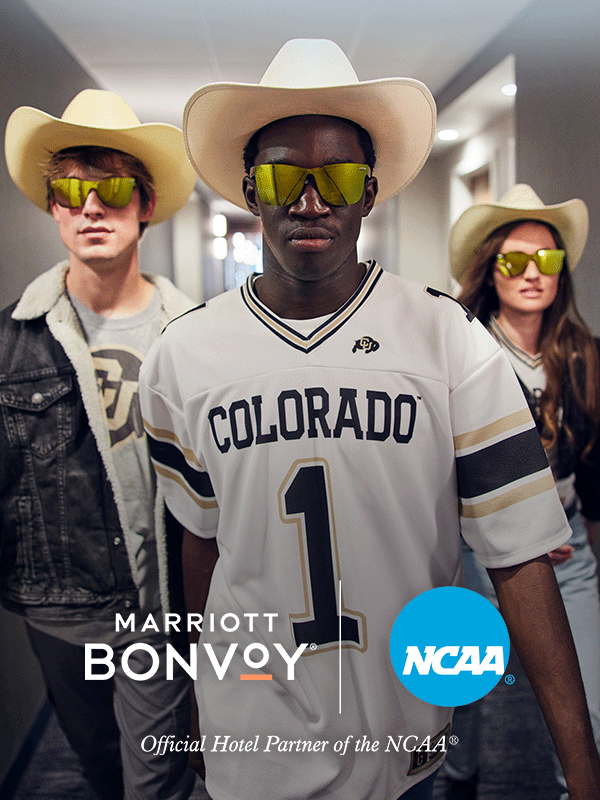 Three sports fams wearing jerseys, cowboy hats, and sunglasses walk through a hotel hallway.