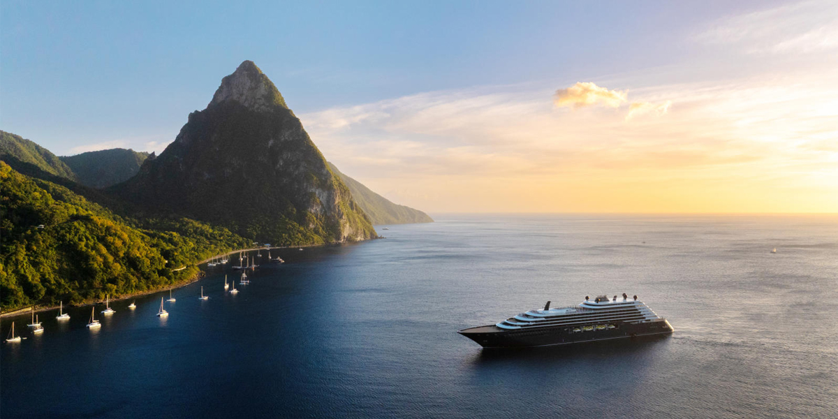 Ilma sails near a lush, mountainous island at sunset.