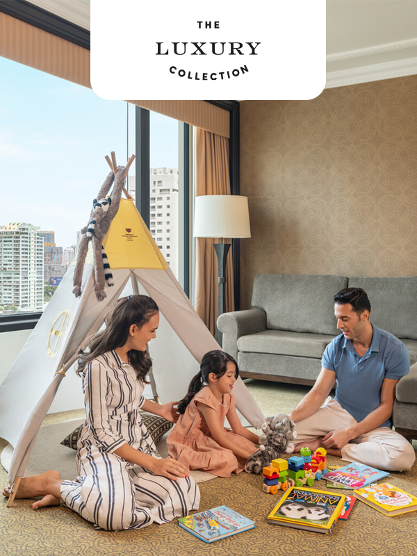 Family playing with toys beside a children’s teepee in a hotel room with city views, under the Sheraton Grande Sukhumvit Bangkok logo.