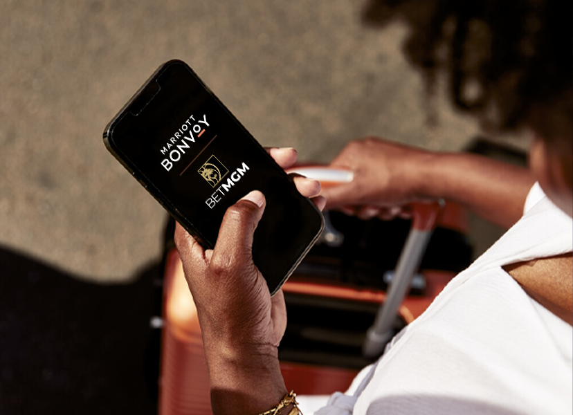 Woman with a roller bag looking down at her phone. Marriott Bonvoy and BetMGM logos are visible on her phone screen.