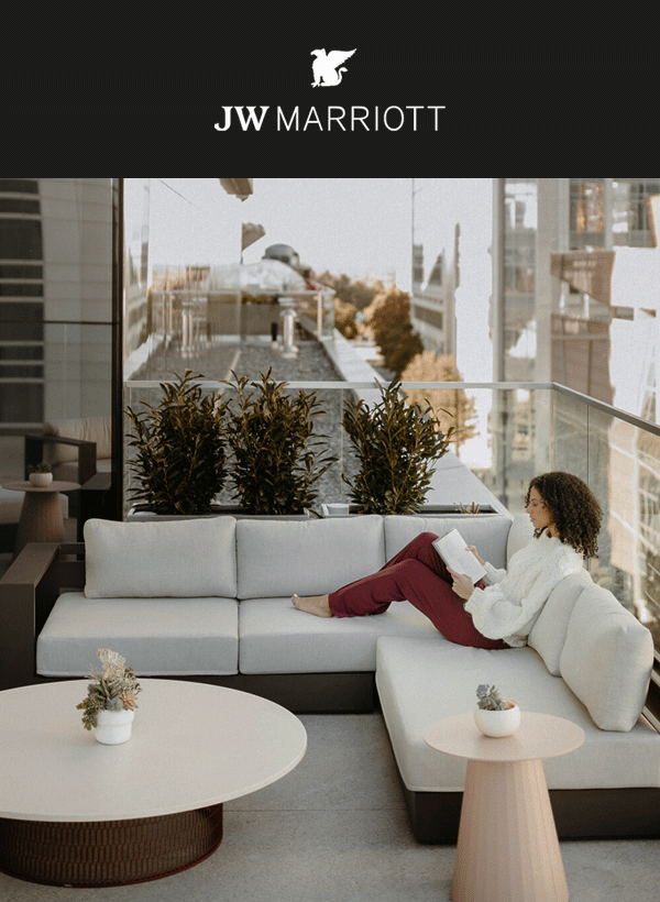 Woman reading a book on a hotel balcony couch.