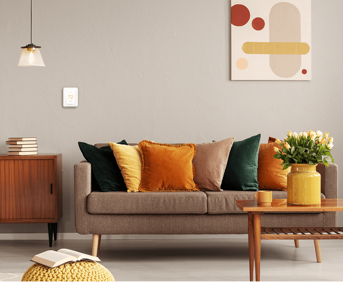 A cozy living room with pillows on a sofa, artwork, and a wall thermostat