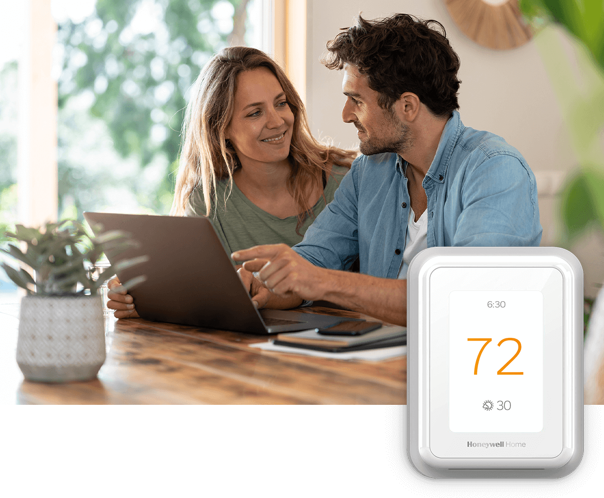 A happy couple smiles at each other while using a laptop together; a thermostat image is in the foreground