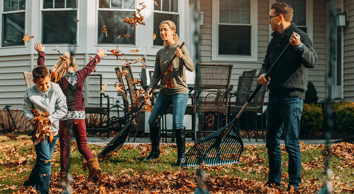 A family enjoys autumn outdoors, raking and playing with leaves
