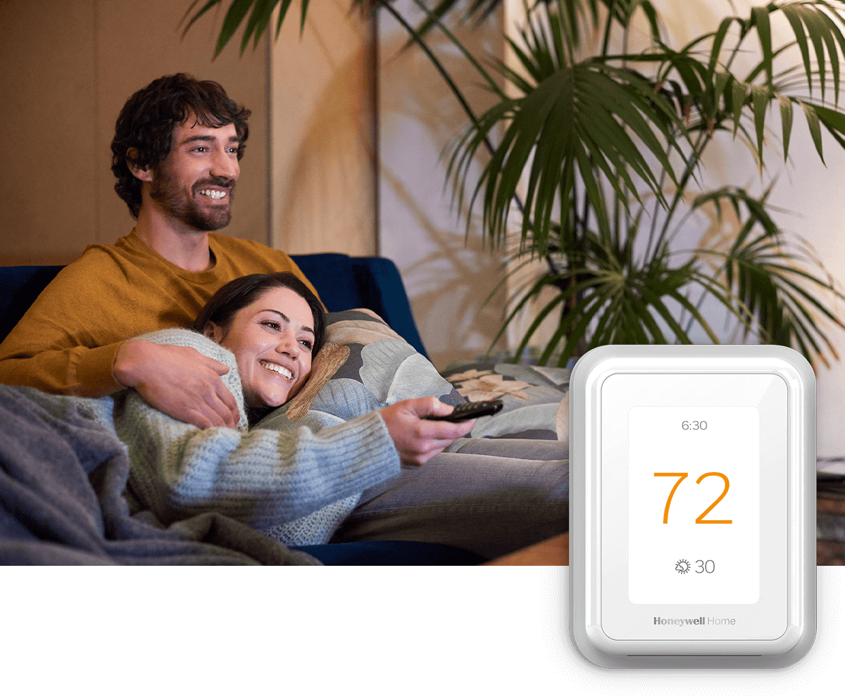 A smiling couple relaxes on the sofa, remote in hand; a thermostat image is in the foreground