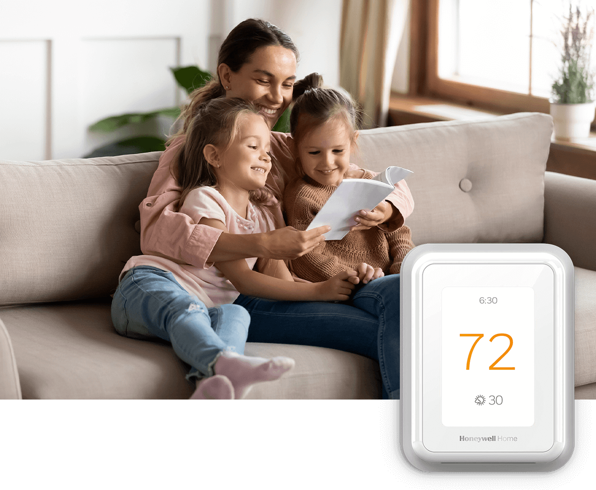 A happy young family sits on couch smiling; a thermostat image is in the foreground