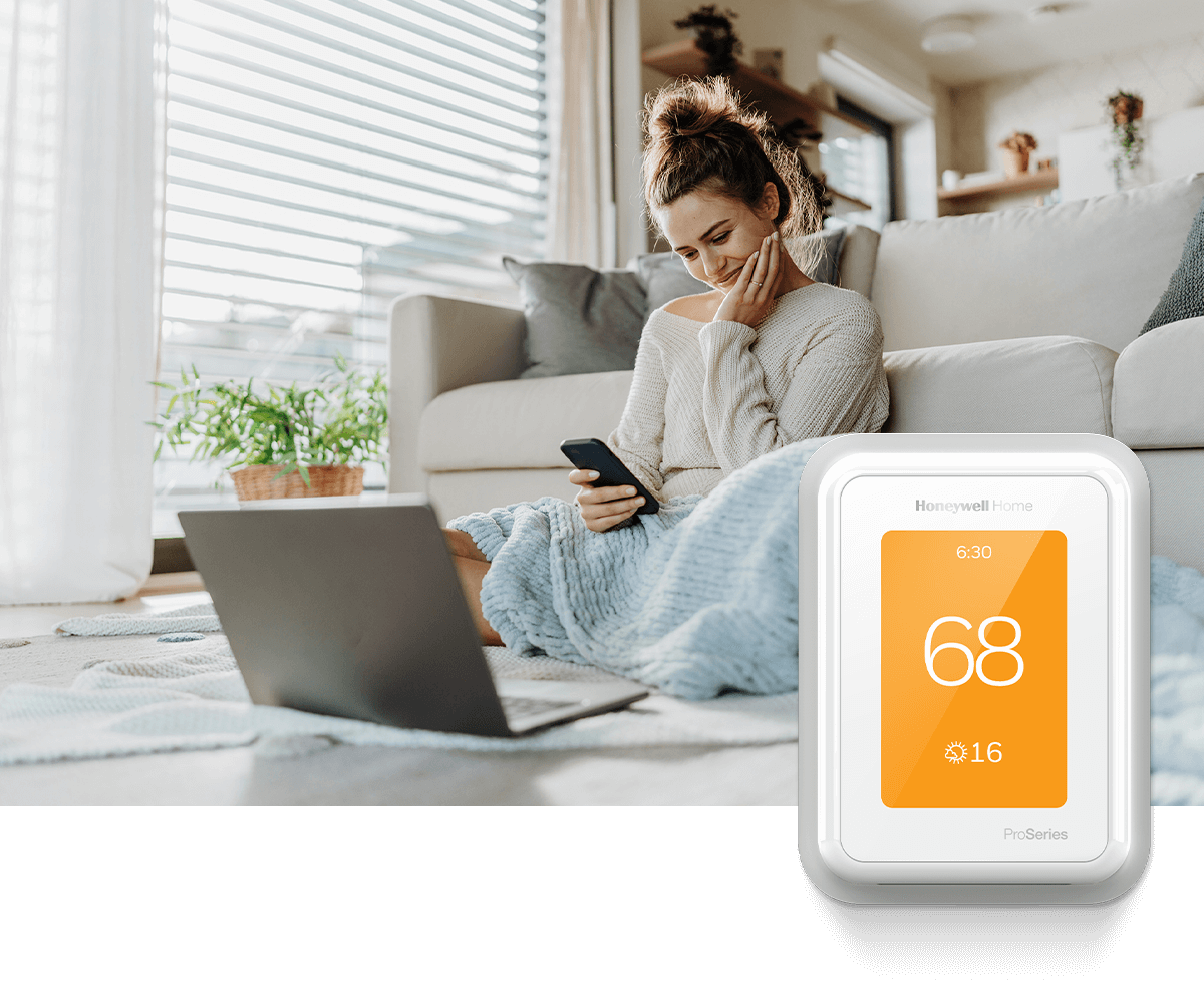 A woman sits in front of a white sofa while looking at her smartphone with a laptop open nearby. In the foreground, a Honeywell Home thermostat shows 70 degrees.
