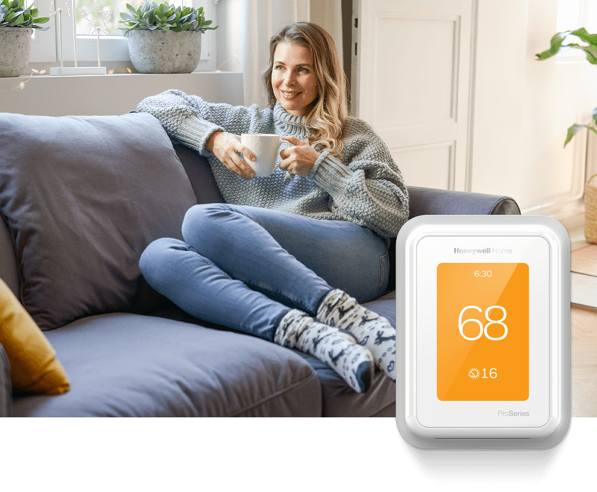 A modern living room is adorned with neutral colors and a single orange pillow. In the foreground a white Honeywell Home thermostat displays 70 degrees.