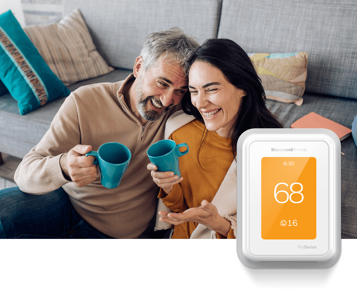 A younger couple shares a laugh over coffee in front of a couch. In the foreground, a Honeywell Home smart thermostat shows 70 degrees.