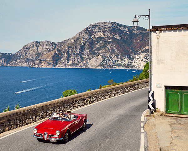 Red car driving though small Italian town.