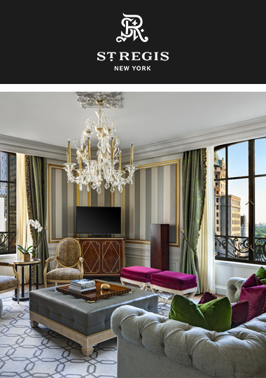 The St. Regis New York suite. An ornate chandlier hangs from the ceiling of the room with traditional furniture, and the view of city skyline can be seen from the window.