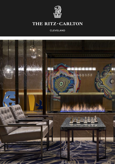 The Ritz-Carlton, Cleveland hotel lobby. Elegant room with plush lounge chairs and a chessboard. A fireplace glows in the background.