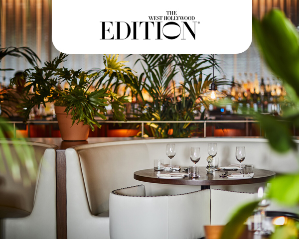 A chic hotel restaurant with a round table set for four, featuring elegant glassware and cutlery. Lush green plants create a serene, upscale ambiance.