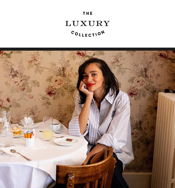 Laila Gohar in elegant attire sits at a table with pastel-colored desserts and a cocktail.