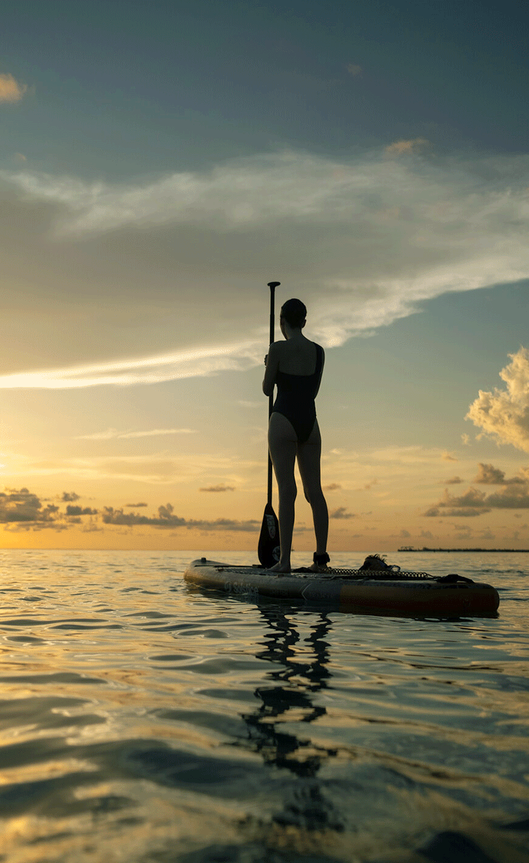 Person standing on a paddleboard during sunset.