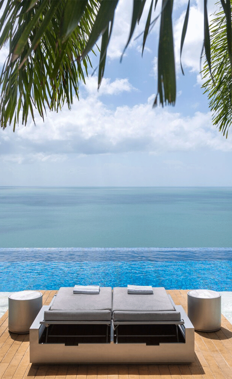 Lounge chairs overlooking a pool and ocean.