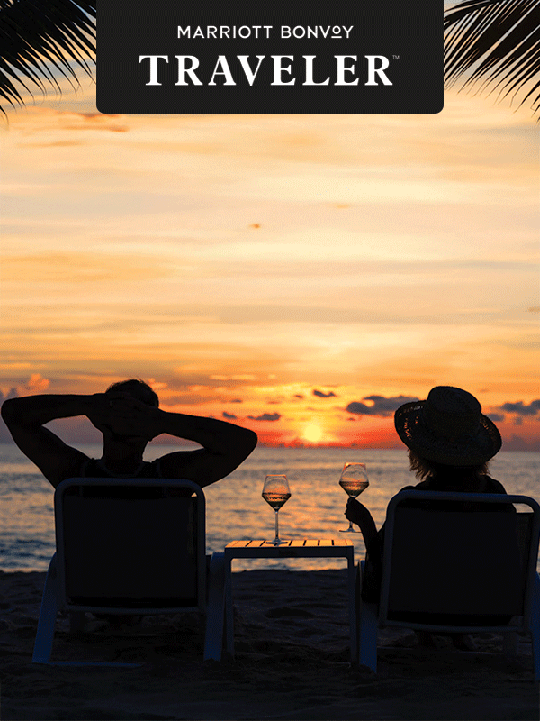 A couple lounges on a beach watching the sunset.