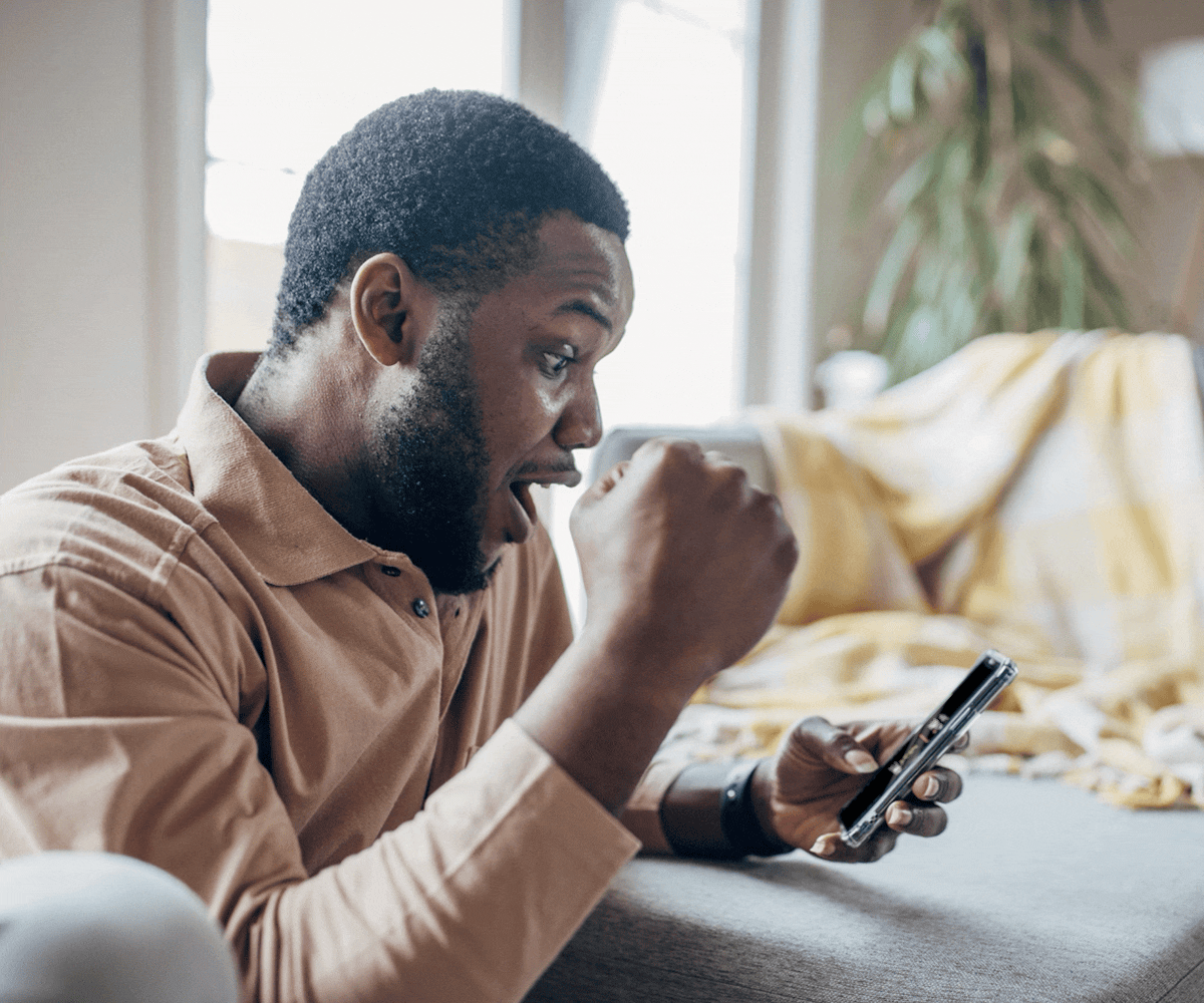 A man on a couch looks excitedly at his phone, fist raised, suggesting a victorious moment. Logos for Marriott Bonvoy and BetMGM are displayed beside him on phone screen.