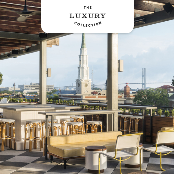 Rooftop terrace with chairs overlooking city skyline and tall church clock tower.
