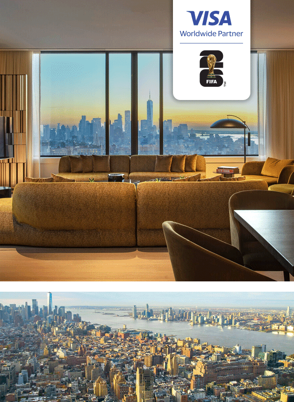 Cozy living room with a large sofa faces floor-to-ceiling windows, offering a stunning view of a city skyline at sunset. Below is an aerial cityscape..
