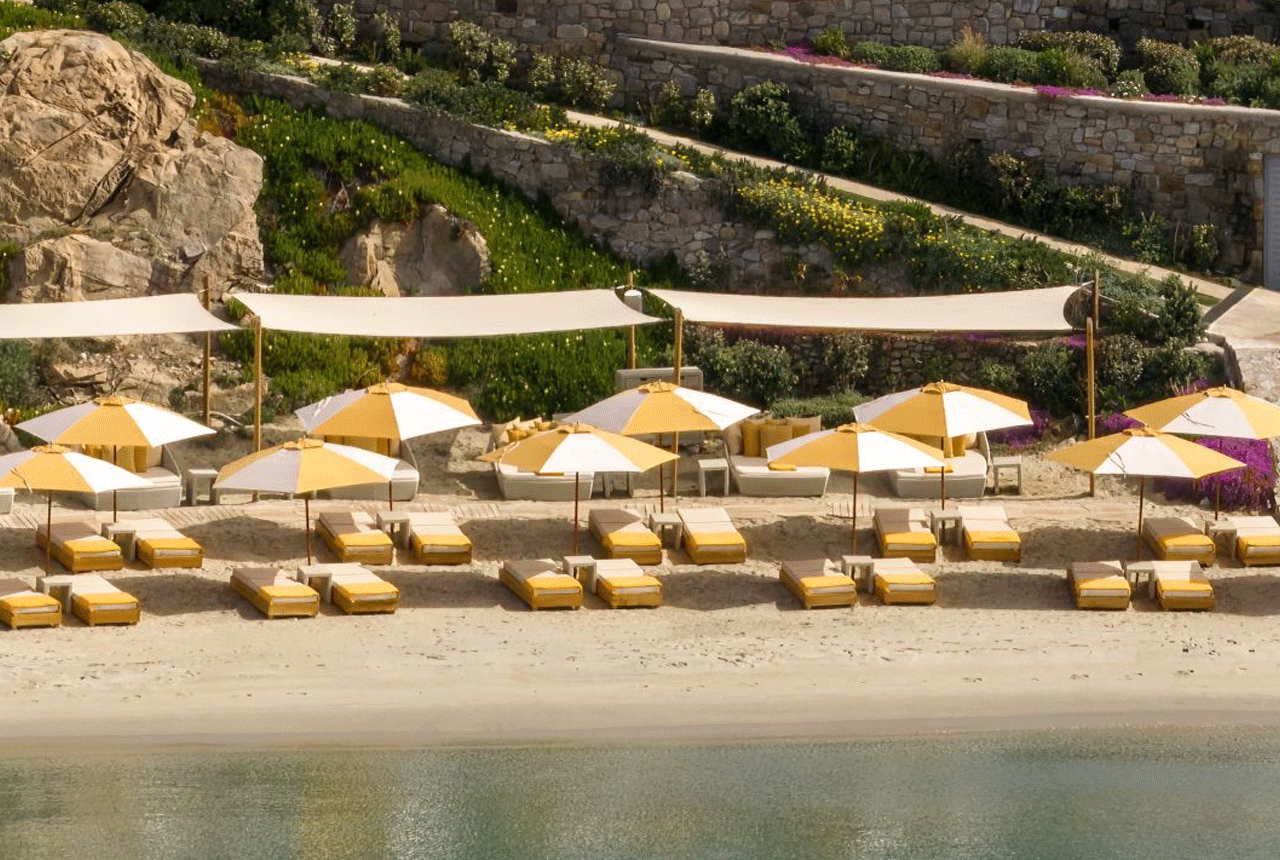 Beach scene with yellow-and-white umbrellas and lounge chairs on sandy shore.