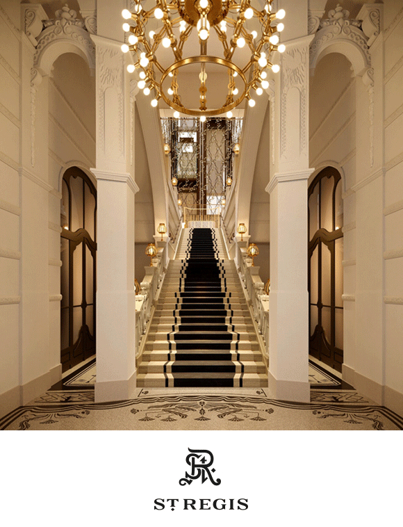 Opulent interior with a grand staircase, ornate chandelier, and symmetrical arches..