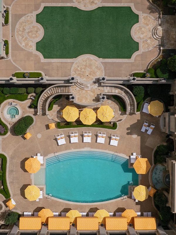 Aerial view of a luxurious pool area with bright yellow umbrellas and lounge chairs surrounding a turquoise pool.