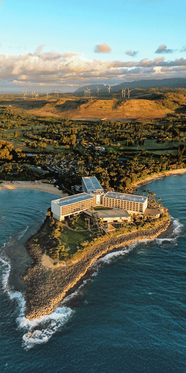 Animated GIF of an aerial view of a coastal resort on a small peninsula surrounded by the ocean and a woman relaxing on a cozy sofa in a sunlit room with large windows, overlooking lush tropical foliage.