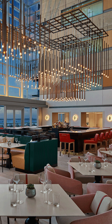 Animated GIF of a chic restaurant interior with modern seating, vibrant colors, and a striking geometric ceiling light and a modern lounge with four curved gray chairs surrounding a round coffee table.